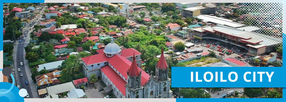 An aerial view of Iloilo City, Philippines, a city with a red roof and Molo Church in the center.