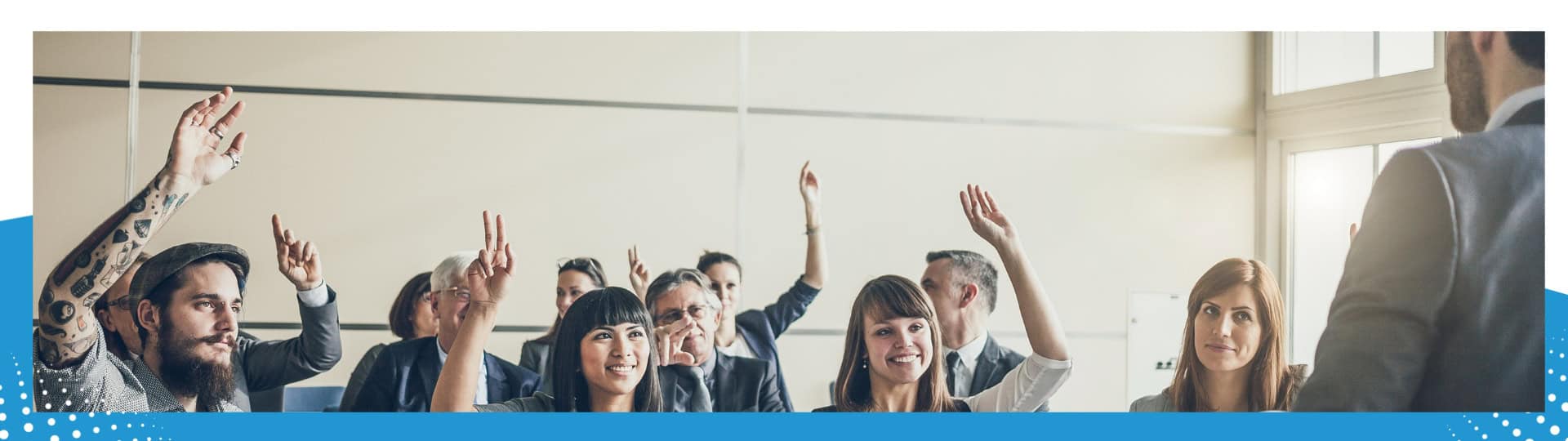 A diverse group of people in a seminar or workshop raising their hands, actively engaging with the speaker, symbolizing participation and learning.