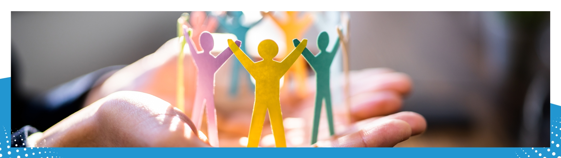 A close-up of hands holding a circle of multicolored paper cutouts of human figures, symbolizing community, diversity, and teamwork