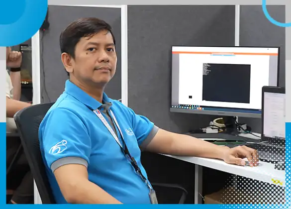 Shore360 IT team member in a blue company-branded shirt seated at a workstation, focused on tasks involving multiple monitors in a professional office setting.