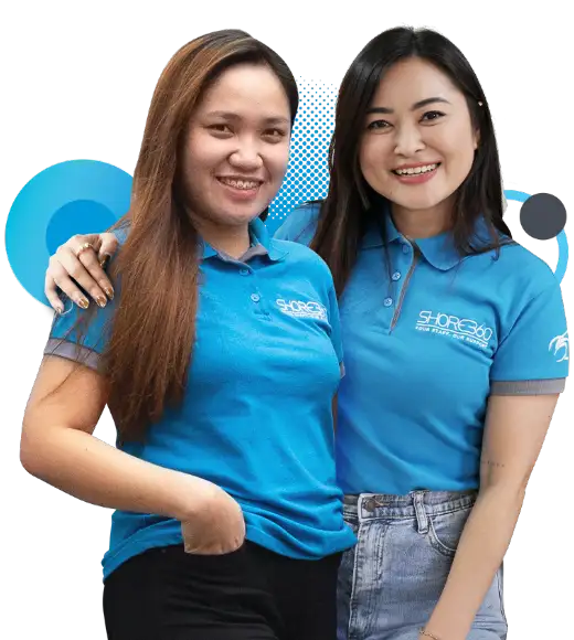 Two Shore360 team members wearing blue company-branded shirts, standing close and smiling confidently, symbolizing teamwork and a friendly workplace culture