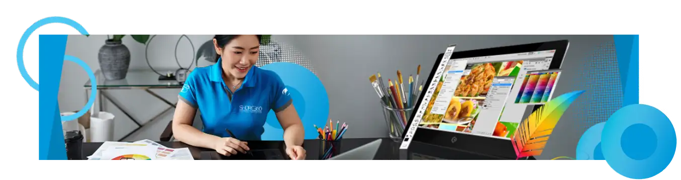 A Shore360 team member working on a graphic design project using digital tools, surrounded by creative materials like color palettes and pencils, with vibrant design work displayed on a monitor.